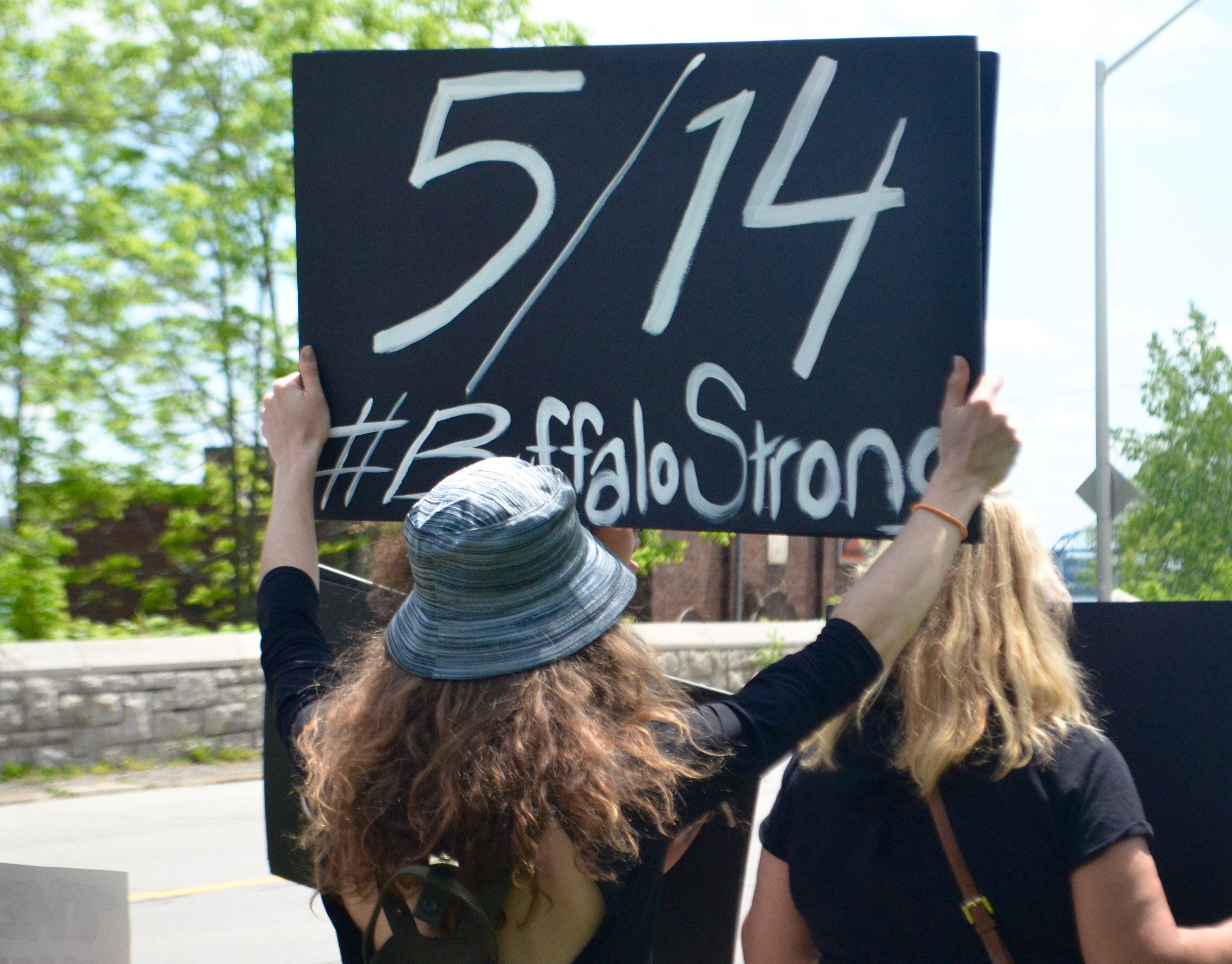 Morgan Hayde carries a sign acknowledging the shooting at a Buffalo supermarket earlier this year that left 10 dead and three others injured.  A manifesto posted online by the alleged shooter, who is currently facing dozens of state and federal charges, made numerous references to the alternative grand conspiracy theory.